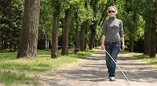 Woman with cane walking along rural sidewalk.