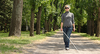 Woman with cane walking along rural sidewalk.
